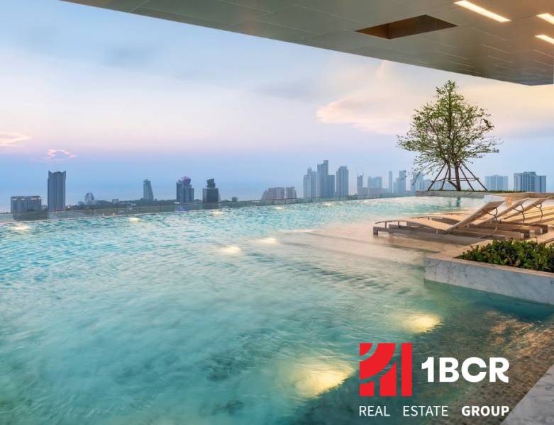 A pool with loungers and a view of the Pattaya city skyline from the apartment construction.