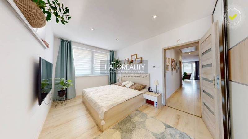 A bedroom in a 3-room apartment with a bed, television, and plants, bright interior.