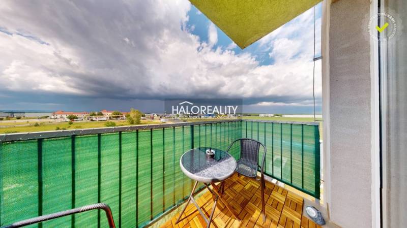 A balcony in a studio apartment with a view of Senec, seating, and a cloudy sky.