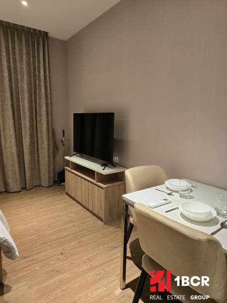 A living space with a television, dining table, and curtains in a studio apartment.