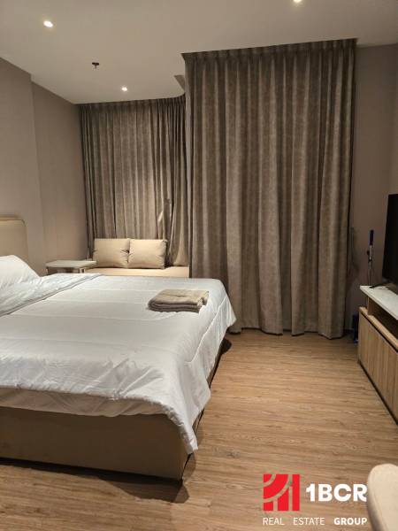 Bedroom in a studio apartment with a double bed, sofa, and curtains.