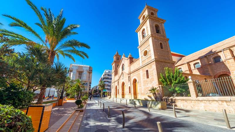 Campoamor Street 12 in Torrevieja with a church and palm trees on a sunny day.