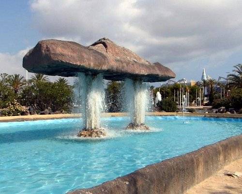 A fountain with an unusual stone structure and water streams in a beautiful setting.