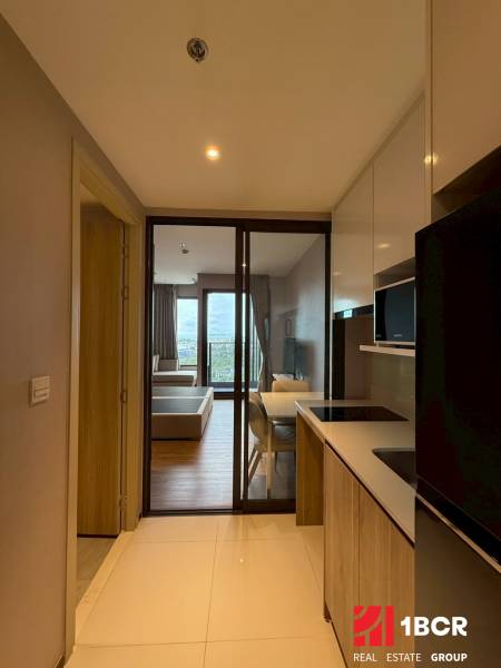 A kitchen in a studio apartment with a view of the living room and balcony.