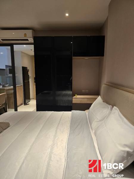 A bedroom with a white bed and a black wardrobe, next to the kitchen unit.