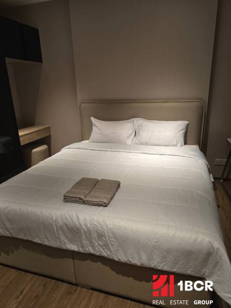 A bedroom in a studio apartment with a large bed and a dresser.