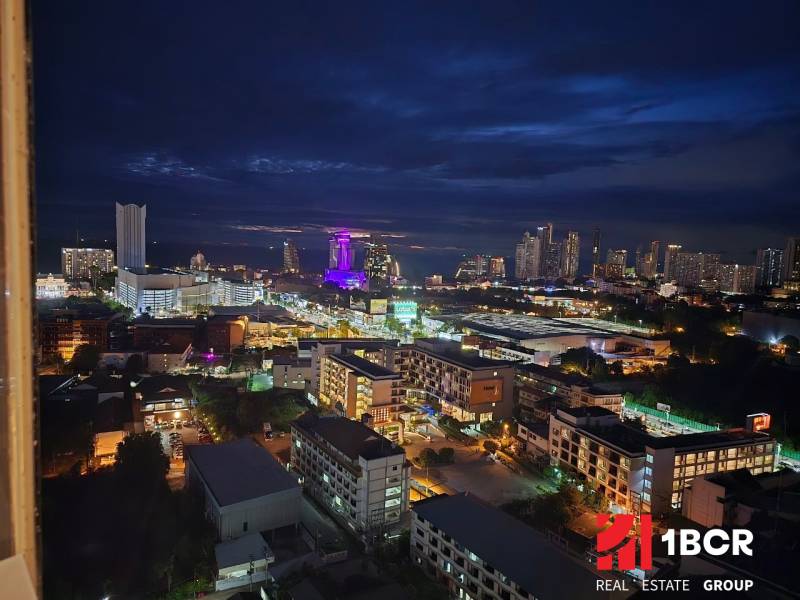 A night view of the city of Pattaya with illuminated buildings and silhouettes on the horizon.