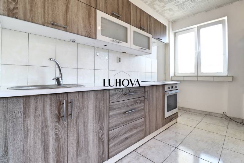 A kitchen in a 2-room apartment with wooden cabinets and white tiles, bright space.