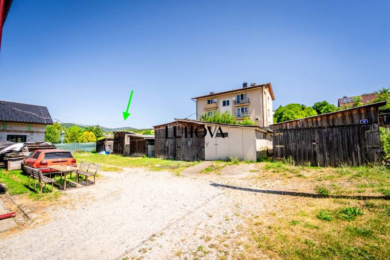 A yard with several wooden buildings and a parked car in Púchov, near a 2-room apartment.