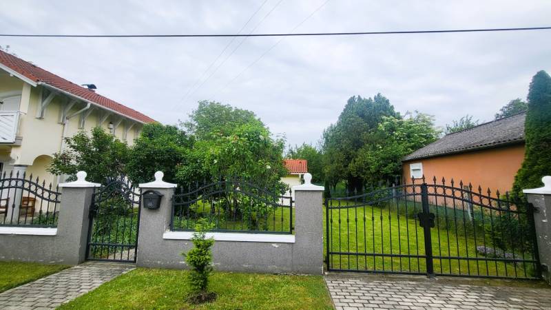 A family house in Dunaszeg with a gate, front garden, and trees.