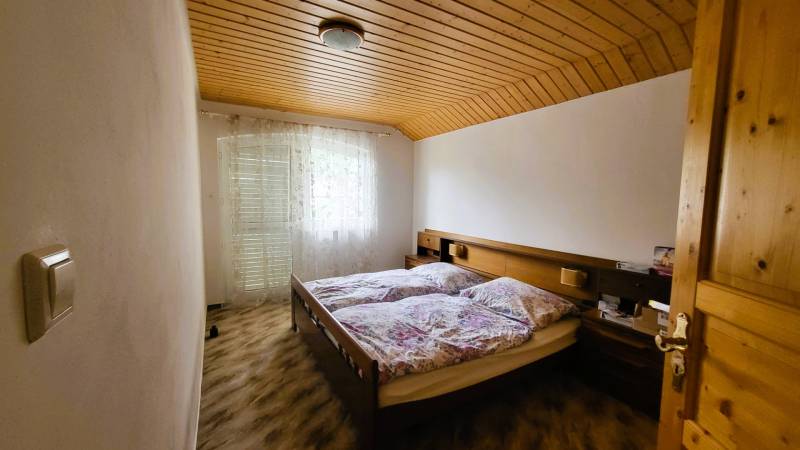 A bedroom in a family house with two beds, a wooden ceiling, and a curtain.