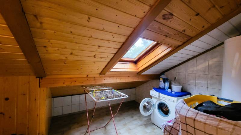 Attic laundry room with a wooden ceiling and a skylight, washing machine, clothes drying rack.