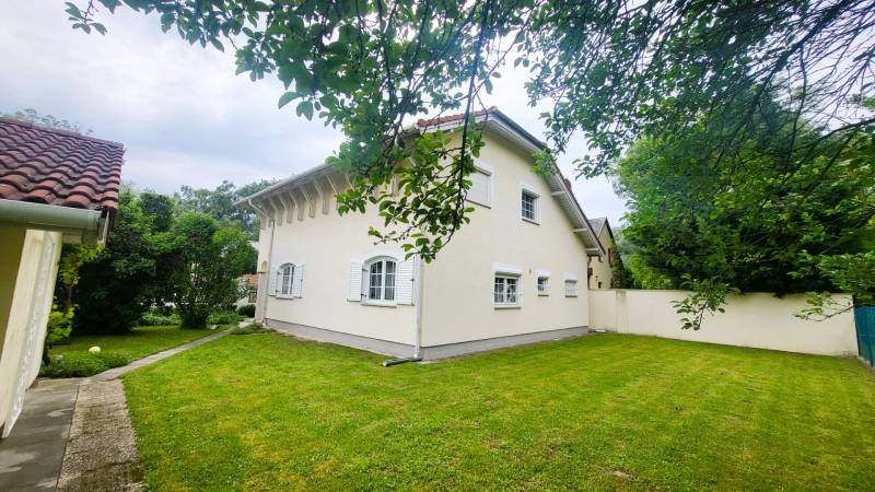 A family house in Dunaszige with a white facade, a landscaped garden, and trees.