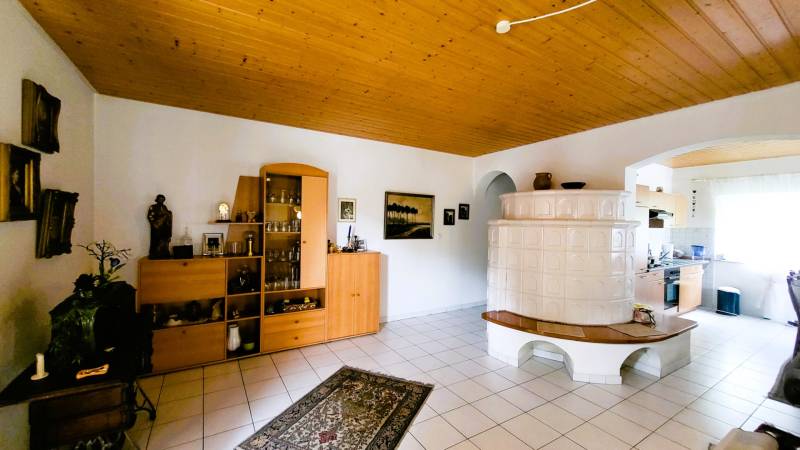 Living room in a family house with a white tiled stove and a wooden ceiling.