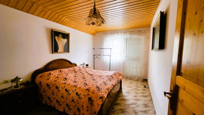 A bedroom in a family house with a wooden ceiling, a painting, and a decorative chandelier.
