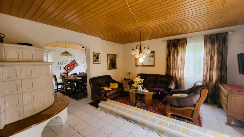 Living room in a family house with a tiled stove, sofa, and dining table.