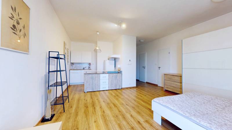 Kitchen corner and bedroom area in a studio apartment, wooden floor and white walls.