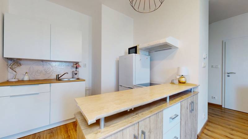 A kitchen in a studio apartment with cabinets, a hood, and a wooden countertop.