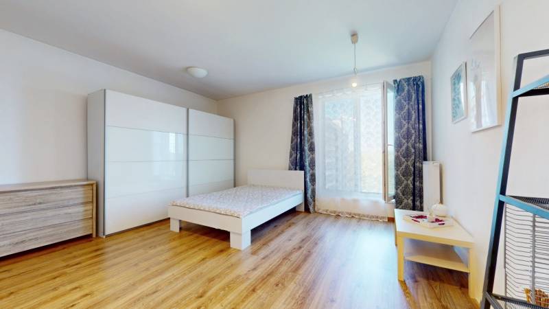 A bright room with a bed, a wardrobe, and a wooden floor in a studio apartment.