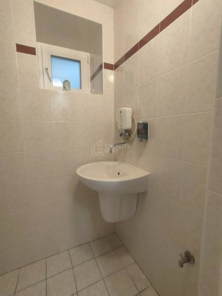 A bathroom with a sink, a window, and a soap dispenser in the tiled area of commercial spaces.