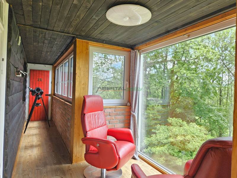 A family house with a glass veranda, red armchairs, a telescope, and a view of the forest.