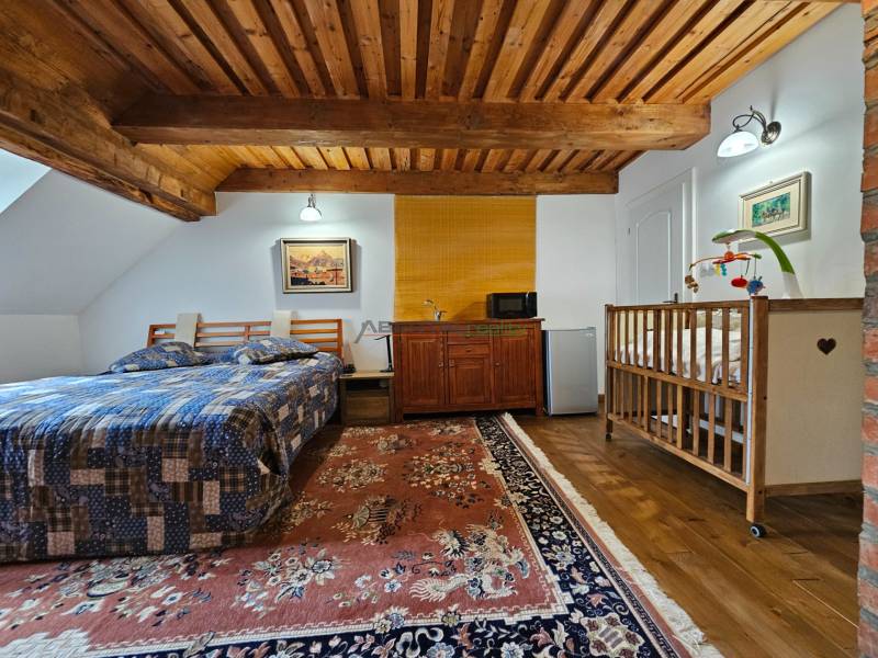 A bedroom in a family house with a wooden ceiling, a bed, a baby crib, and a carpet.