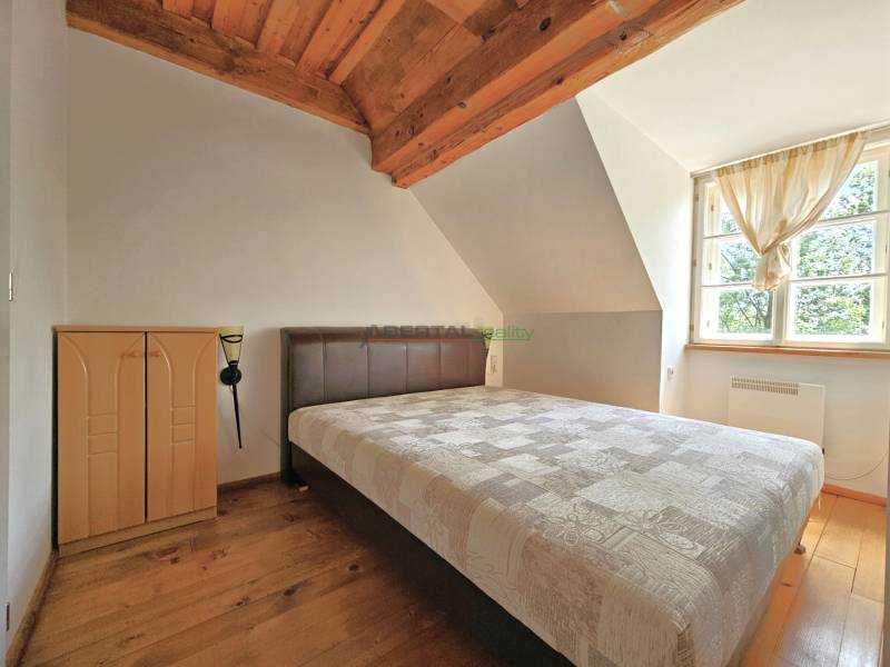 Attic bedroom in a family house with roof beams and a large window.