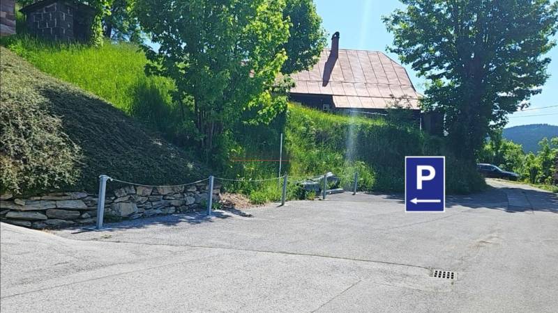 Parking lot on Donovaly Street in the town of Donovaly near family houses, with trees and grass.