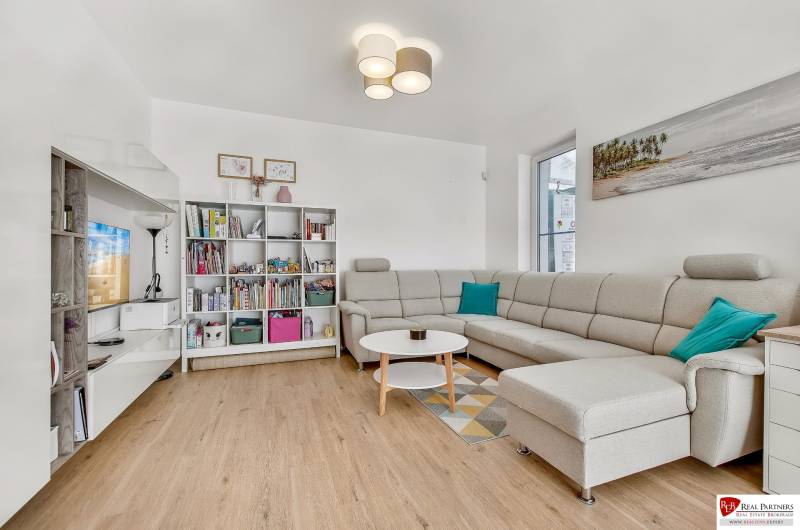 Living room in a family house with a sofa, bookshelf, and table on a wooden floor.