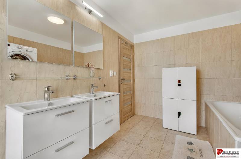 A bathroom in a family house with a double sink, white cabinet, and bathtub.