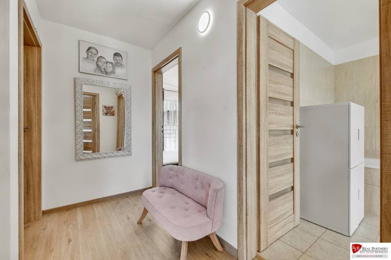 A hallway in a family house with a pink bench, a mirror, and wooden doors.
