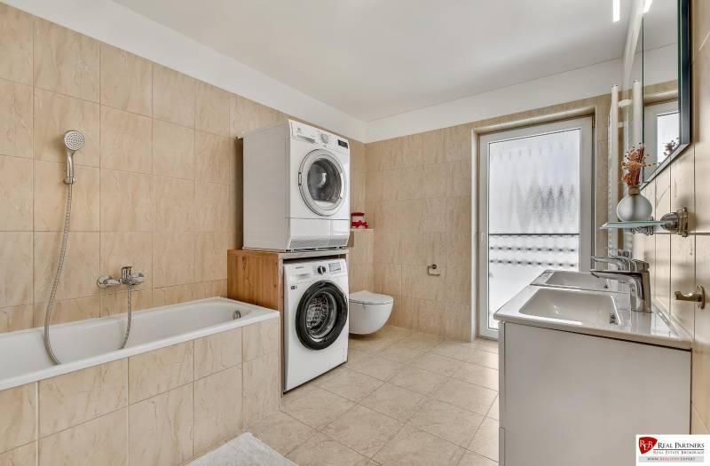 A bathroom in a family house with a bathtub, washing machine, dryer, and double sink.