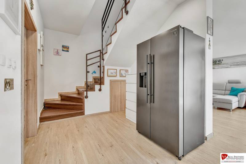 A refrigerator in the hallway of a family house with a wooden staircase and decorations on the walls.
