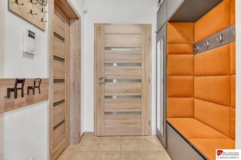 The entrance hall in the family house with an orange bench, wooden doors, and wall hooks.