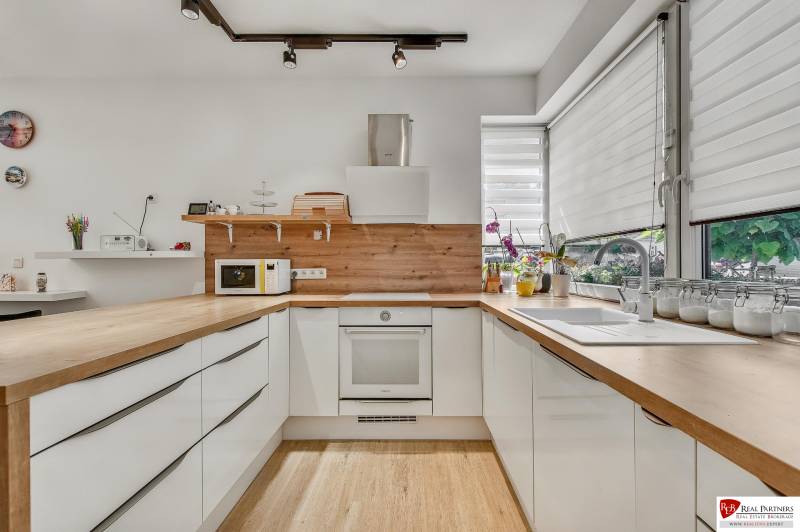 A kitchen in a family house with light cabinets, a wooden countertop, and large windows.
