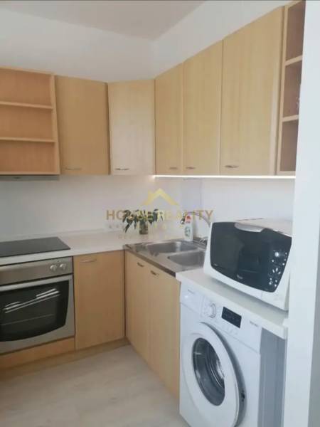 A kitchen in a studio apartment with a stove, sink, washing machine, and microwave.