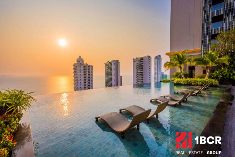 Pool, loungers, and the panorama of apartment construction in Pattaya at sunset.