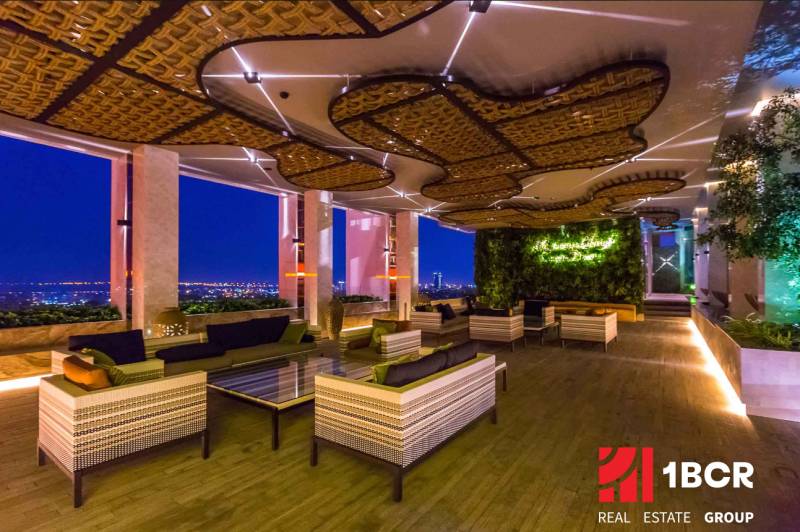 Luxury apartment space with a view of the city's evening lights, a green wall, and comfortable seating.