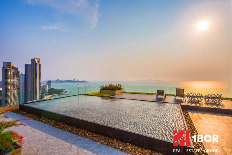 Apartment construction in Pattaya with a rooftop pool and sea view at sunset.