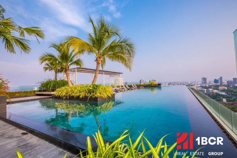 Infinity pool and palm trees on the rooftop with a view of the city skyline in Pattaya, apartment construction.