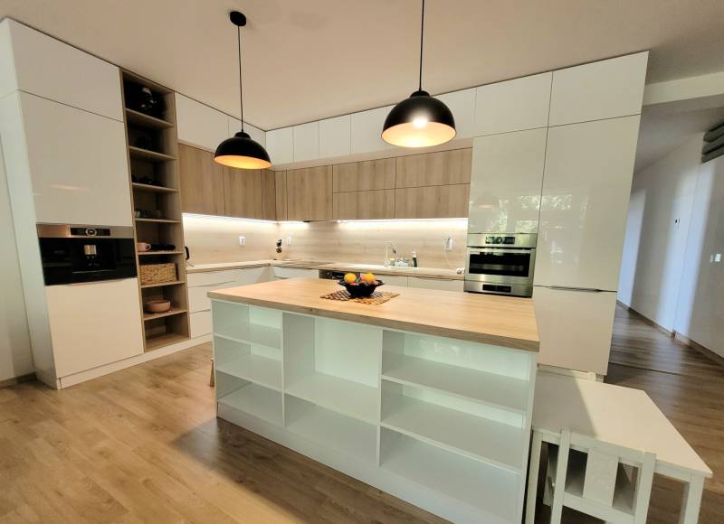 A kitchen in a 3-room apartment with an island, wooden details, and built-in appliances.
