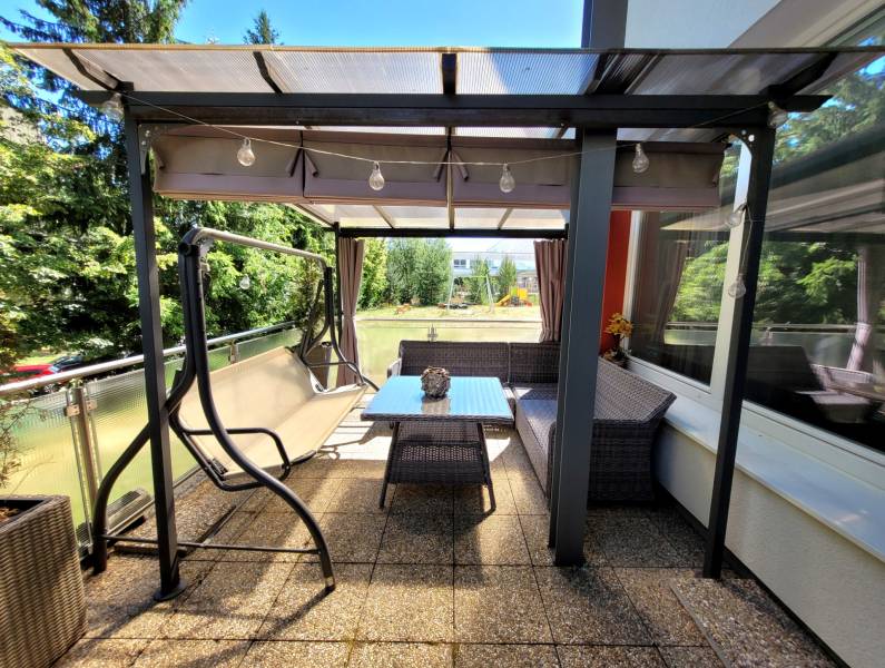 Terrace of a 3-room apartment in Banská Bystrica with a swing and a table for sitting.