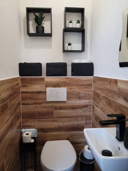 A toilet in a 3-room apartment with wooden paneling and black accessories.