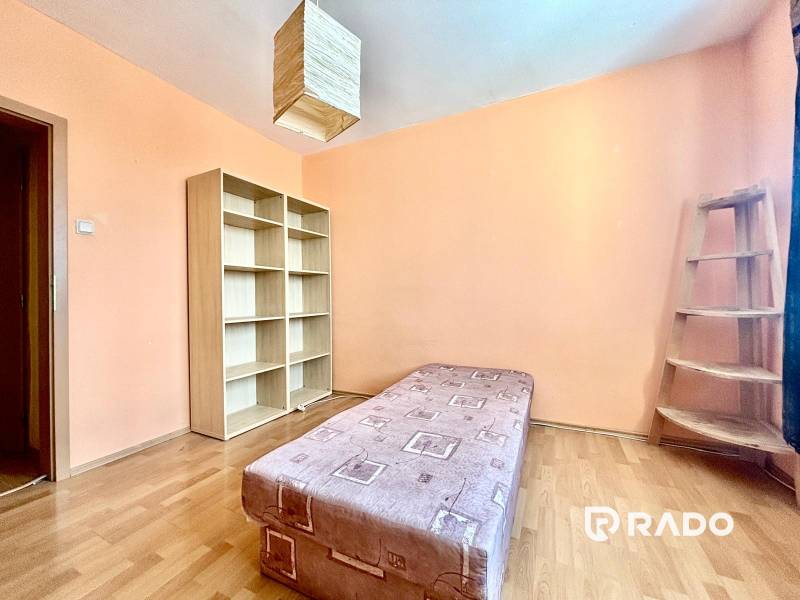 A room in a 3-room apartment with a bed, shelves, and wooden stairs.
