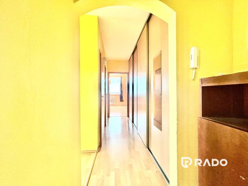A narrow hallway with built-in wardrobes in a three-room apartment with wooden paneling.