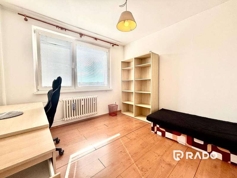 A room with a table, a chair, a shelf, and a bed in a three-room apartment.