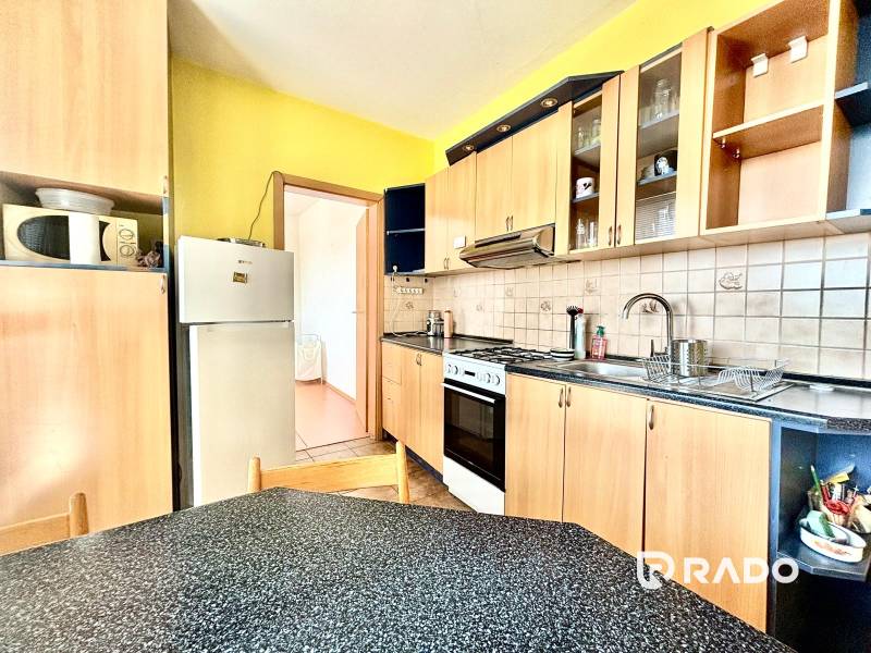 A kitchen in a 3-room apartment with wooden cabinets, a stove, and a refrigerator.