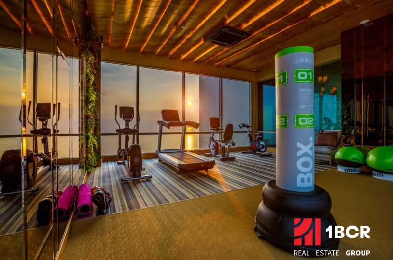 A fitness center with a view of the sunset through large windows, apartment construction.