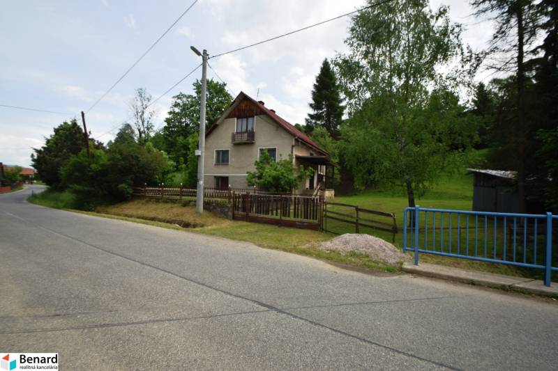 A family house in Veľká Lesná by the road, surrounded by greenery and a fence.