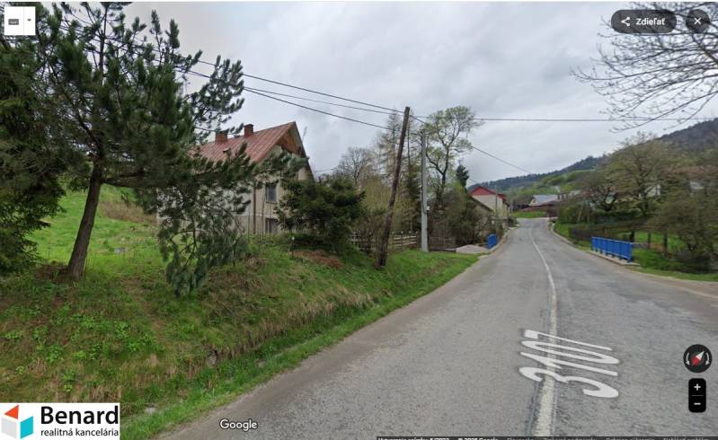 A road by a family house in the village of Veľká Lesná, surrounded by greenery and trees.
